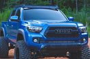 Lifted blue 3rd Gen Toyota Tacoma with a roof rack parked on a dirt trail in the woods